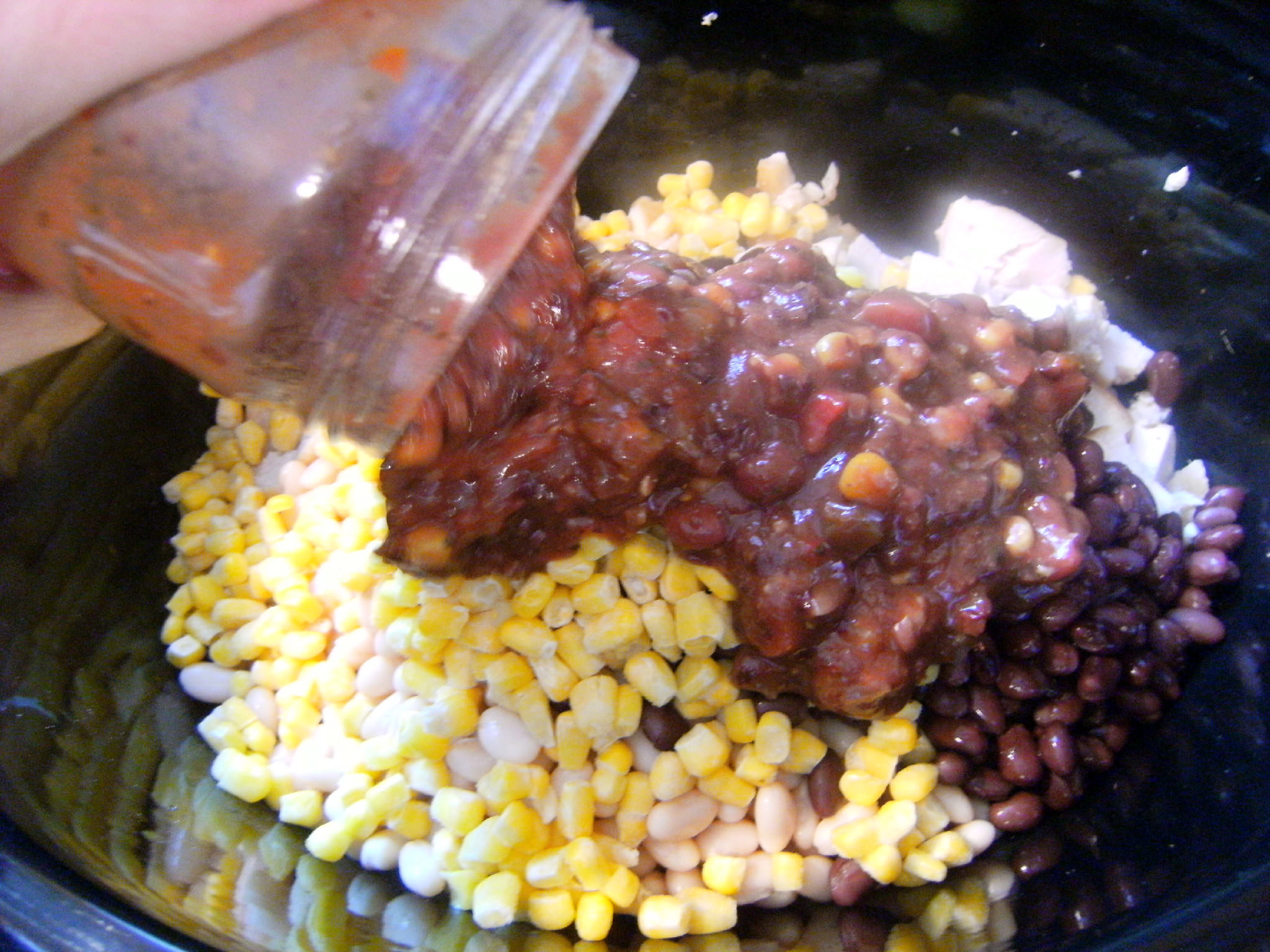 adding ingredients to make a slow cooker chicken chili recipe
